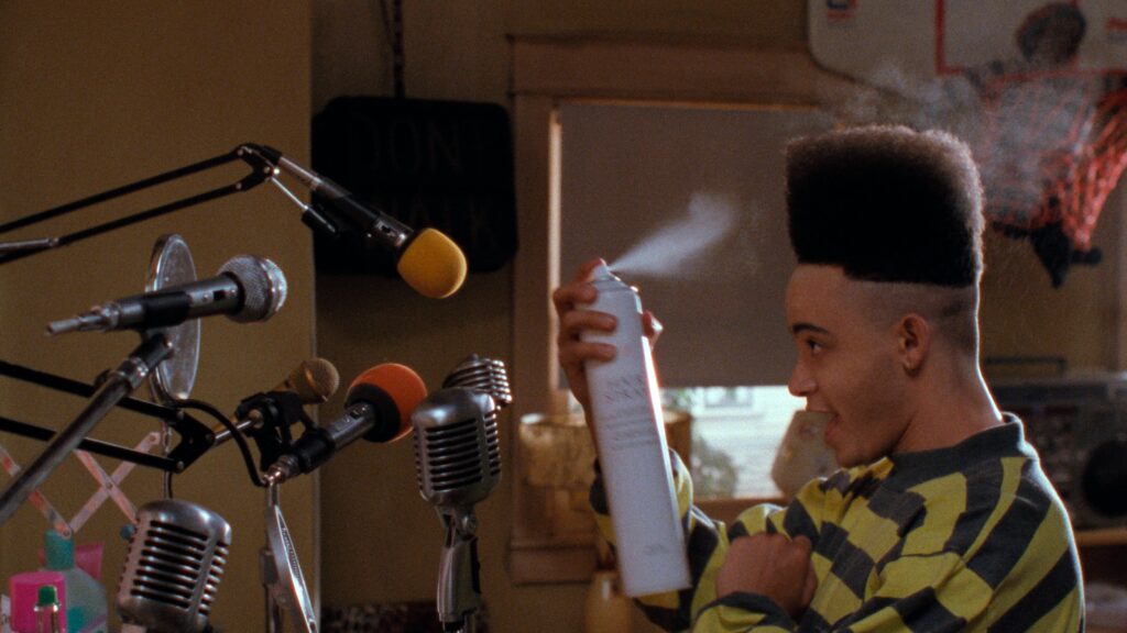 Christopher "Kid" Reid sprays an aerosol can on his hi-top fade in front a number of microphones